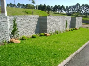 muro construido com pedra basalto na cidade de parai, conta com uma grama verde e arvores.